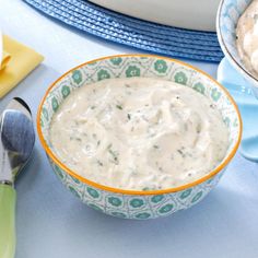 a bowl of dip sits on a blue table cloth next to two bowls of food