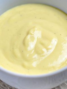 a white bowl filled with yellow sauce on top of a wooden table