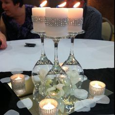 three candles are lit in front of two wine glasses on a table with white flowers