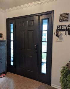 a black front door with two sidelights in a white room next to a dresser