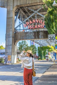 a woman standing on the side of a road in front of an old train bridge