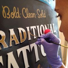 a woman in purple gloves painting the letters on a blackboard with gold lettering and a red ball