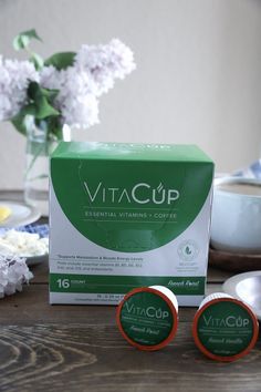 two boxes of vitacupp sitting on a table next to some plates and flowers