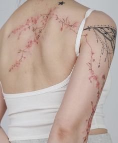 the back of a woman's shoulder with tattoos on her left arm and pink flowers