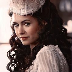 a woman with curly hair wearing a feathered hat