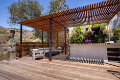 a wooden deck with an outdoor grill and seating area next to the patio is covered by a pergolated roof