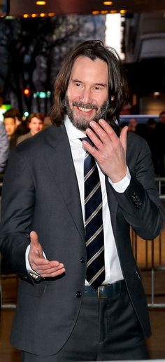 a man in a suit and tie holding his hand up to his mouth while standing on a red carpet