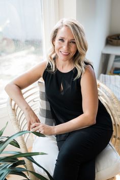 a woman sitting on a chair in front of a window with a potted plant