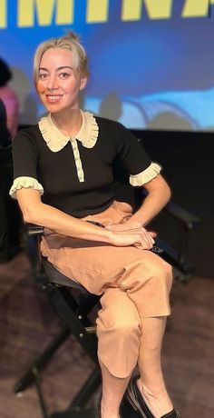 a woman sitting on top of a chair in front of a screen with her legs crossed