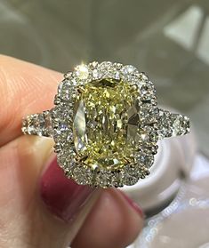 a fancy yellow diamond ring is being held by someone's hand in front of the camera