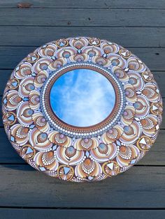 a decorative mirror on the side of a wooden deck with blue sky in the background