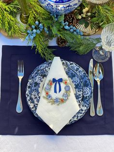 a place setting with blue and white plates, silverware, napkins and pine cones