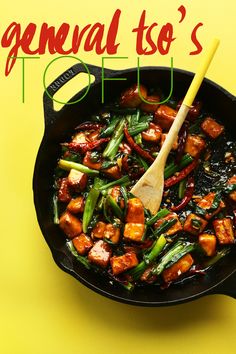 a pan filled with meat and vegetables on top of a yellow table next to a wooden spoon