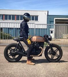 a person sitting on top of a motorcycle in front of a building with a fence