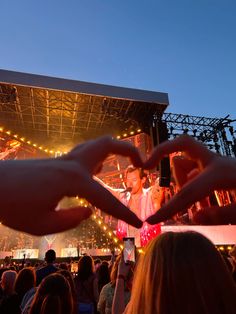 two hands making a heart shape in front of a stage with lights and people holding up their cell phones