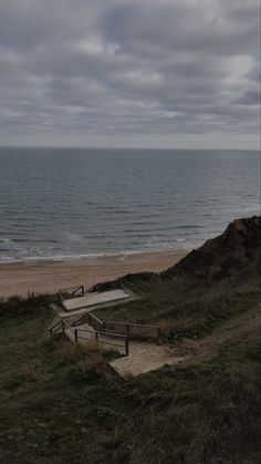 two wooden benches sitting on top of a grass covered hillside near the ocean and beach