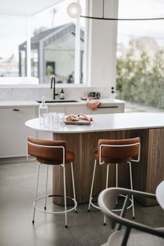 two stools sit at the center of a kitchen island in front of an open window