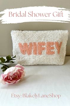 a white pillow with the word wife on it and a pink flower in front of it