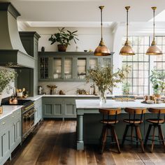 a kitchen with wooden floors and green cabinets, white counter tops and gold pendant lights hanging from the ceiling