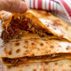 a hand holding a tortilla with meat and cheese