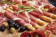 an assortment of meats and olives on a cutting board