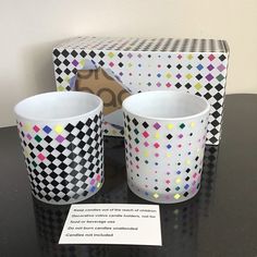 two cups sitting on top of a black table next to a box with a sign