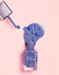 a bottle of dior nail polish sitting on top of a pink background with blue flowers