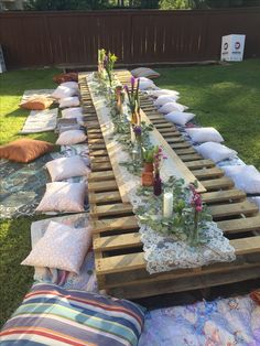 a long table is set up with pillows and flowers on the grass in front of it