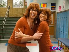 two women hugging each other in the middle of a room with lockers and stairs