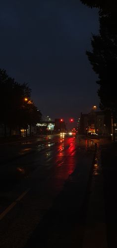 a city street at night with cars driving down the road and lights reflecting on the wet pavement