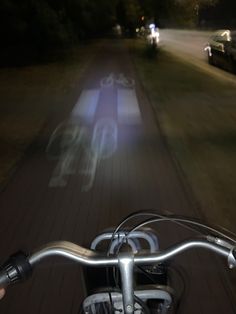 a person riding a bike down a street at night with headlights shining on the road