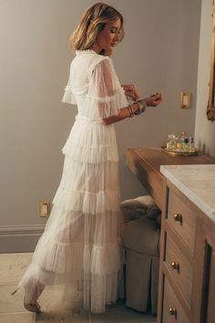 a woman standing in front of a mirror wearing a white dress with tiered layers