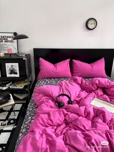 a bed with pink sheets and headphones on it next to a black shelf filled with books