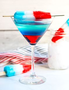 a red, white and blue drink in a martini glass next to marshmallows