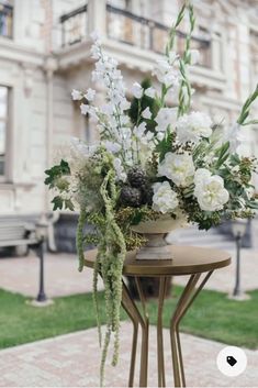 a vase with white flowers sitting on top of a table next to a bench in front of a building