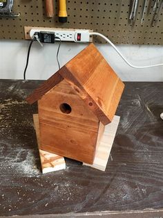 a wooden birdhouse sitting on top of a piece of wood in front of a workbench