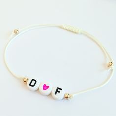 a white string bracelet with the word dof written on it and a pink heart