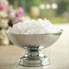 a silver bowl filled with white flowers on top of a table