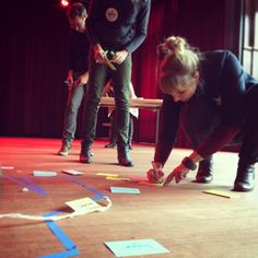 three people are standing on the stage and one person is drawing something with blue tape