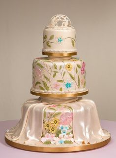 a three tiered wedding cake with flowers on it's sides and gold trim