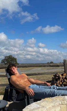 a shirtless man sitting in a chair next to a pile of wood and firewood