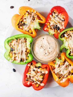 stuffed bell peppers are arranged on a plate with a dip in the middle and toppings