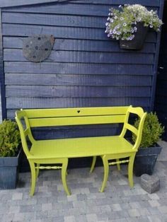 a yellow bench sitting in front of a blue wall with potted plants on it