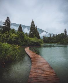 a wooden walkway leading to a lake with mountains in the background and foggy sky