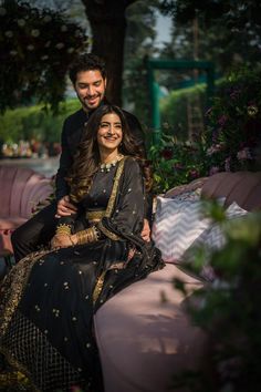 a man and woman sitting on top of a pink couch in front of a tree