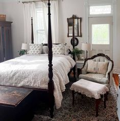 a bedroom with a four post bed, chair and ottoman