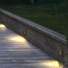 the light shines on the wooden walkway beside the grass and trees in the background