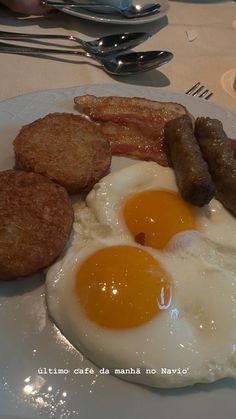 an egg, sausage and fried eggs on a white plate with silverware at a restaurant