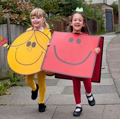 two girls in costumes holding up large pieces of paper with faces on them and smiling