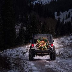 a jeep with a christmas tree on the back driving down a snowy road at night